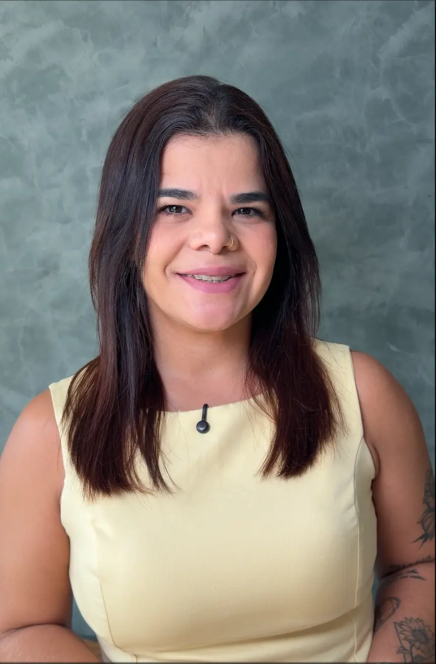 Retrato de Giorggia Cardoso sorrindo, com blusa amarela, diante de uma parede verde